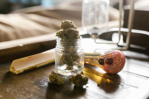 Container of cannabis next to rolling paper and a pipe